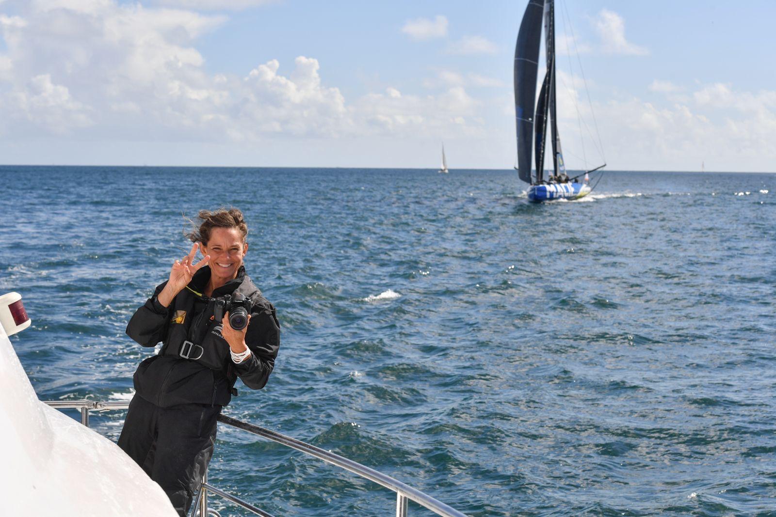 Femme souriante avec un appareil photo à bord d'un voilier lors d'une régate à Lorient