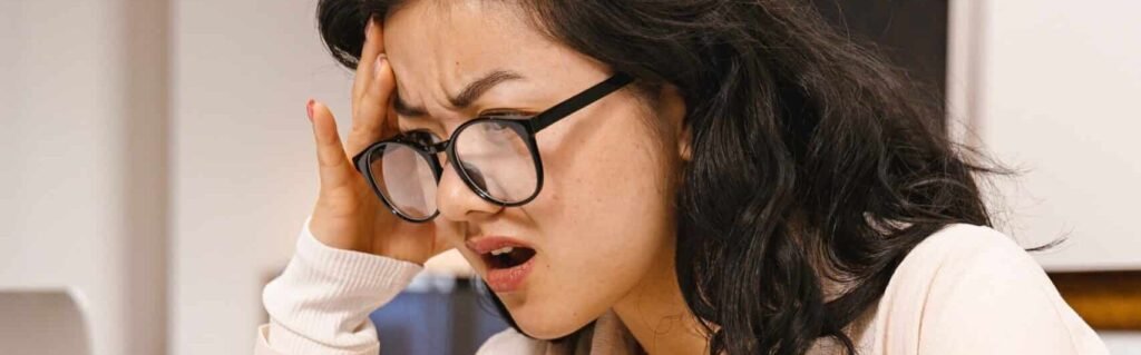 Femme agacée devant son ordinateur portable, main sur la tempe, pour illustrer les expressions pour râler en français